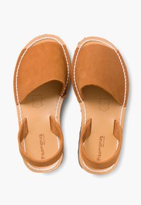 Brązowe zamszowe sandały z odkrytymi palcami i piętą, z białymi przeszyciami oraz płaską podeszwą. Wydrukowane logo na wkładce.