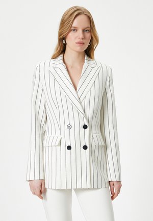 Blazer doppiopetto bianco con righe nere, caratterizzato da un rever a punte, due tasche frontali e bottoni neri.