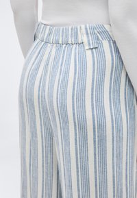 Κοντινό πλάνο ενός ατόμου που φοράει παντελόνι ψηλόμεσο με κάθετες μπλε και άσπρες ρίγες και ελαστική μέση, σε συνδυασμό με ένα λευκό μπλουζάκι.