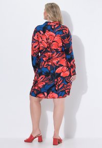 Kukkamekko punaisena, sinisenä ja mustana, pitkillä hihoilla, kapea vyötärö ja polvipituinen helma. Yhdistetty punaisiin paksupohjaisiin sandaaleihin.