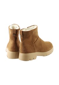 Une paire de bottines en daim beige avec des semelles épaisses beiges et une doublure en fausse fourrure blanche, montrée d'un angle arrière sur un fond blanc.