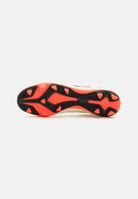 Bota de fútbol con una suela negra y naranja. Presenta un agarre texturizado y un diseño angular, con tacos prominentes para mayor tracción.
