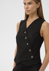 Črna brezrokavna majica z ovijajočim dizajnom, ki vključuje pet dekorativnih gumbov, gladko teksturo in prilegajoč silhueto.