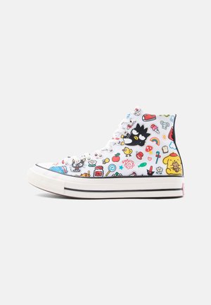 Witte hoge sneaker met kleurrijke cartoonfiguren, waaronder een zwarte vogel, een gele hond, fruit en verschillende speelse iconen op de stof.