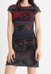 Robe longueur genou en tissu texturé, avec un fond noir orné de motifs floraux et géométriques colorés sur le corsage et l'ourlet.