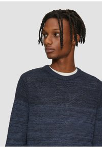Granatowy sweter dzianinowy z okrągłym dekoltem, zdobiony teksturowymi wzorami i różnymi odcieniami niebieskiego, wykonany z miękkiej mieszanki tkanin.