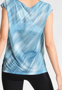 Modrý vzorovaný top s krátkými rukávy, volným střihem, jemnou texturou a zaobleným lemem. Design zahrnuje plynulý, abstraktní vzor.