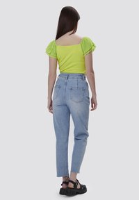 Top verde lima con mangas cortas plisadas, combinado con jeans de tiro alto en azul claro con dobladillo deshilachado, y sandalias de plataforma negras.