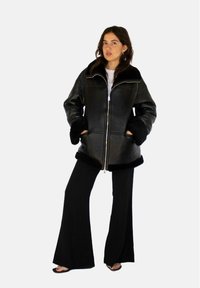 Zwarte leren jas met schapenwollen accenten, voorzien van een ritsluiting en twee voorzakken. Flared zwarte broek maakt de outfit compleet.