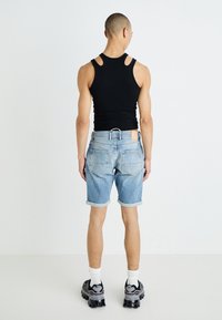Un débardeur noir avec découpes, un short en denim bleu clair avec des ourlets retroussés et des baskets noires à semelles texturées, se tenant sur un fond blanc.