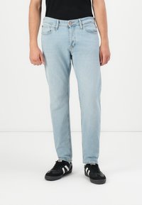 Jeans de mezclilla azul claro con corte recto, diseño de cinco bolsillos y costuras en contraste, combinados con zapatillas negras con rayas blancas.