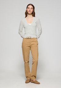 Cárdigan ligero de crema con cuello en V y cierre de botones, combinado con pantalones chinos color canela y zapatos de lona beige, presentando un atuendo casual.