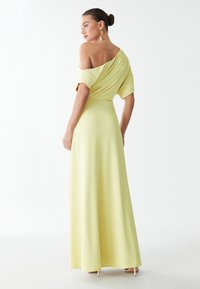 Robe maxi jaune, décolletée sur les épaules, avec un tissu drapé, une jupe fluide et une texture lisse. Dotée de manches courtes et de détails subtils au dos.