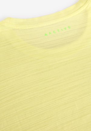T-shirt d'athlétisme jaune citron, tissu léger avec une texture subtile, doté d'un col rond et du mot « ACTIVE » imprimé en vert dans le dos.