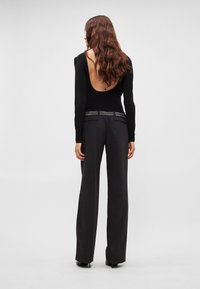 Μαύρο μακρυμάνικο τοπ με βαθύ άνοιγμα στην πλάτη, σε συνδυασμό με παντελόνι ψηλόμεσο, φαρδύ στο πόδι, σε σκούρο γκρι χρώμα με ζώνη διακοσμημένη με τρουκς.