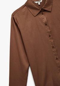 Brązowa koszula z długim rękawem, wykonana z gładkiego materiału, z kołnierzykiem, z siedmioma guzikami z przodu i lekko zaokrąglonym dołem.