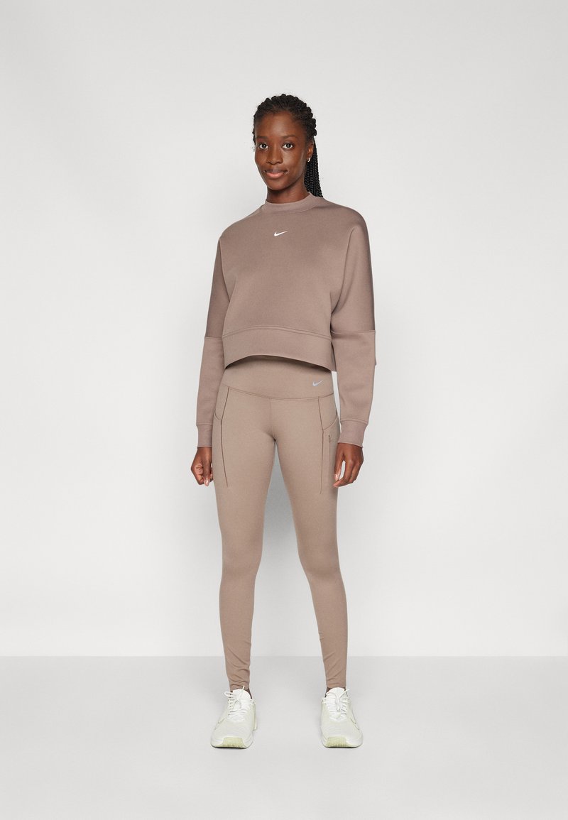 Bruine cropped sweatshirt met een klein logo, gecombineerd met bijpassende leggings met zijzakken en een slim fit. Sportieve witte schoenen.
