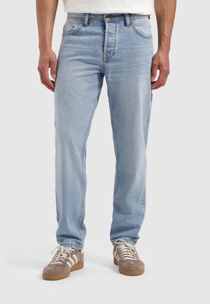 Lichtblauwe denim jeans met een ontspannen pasvorm, met vijf zakken, subtiele vervaging en contrasterend stiksel, gecombineerd met bruin suède sneakers.