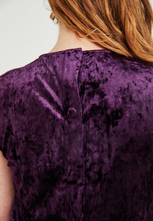 Nærbillede af en person med lysebrunt hår iført en lilla crushed velvet top, med fokus på stofets tekstur og ryggen af halsudskæringen.