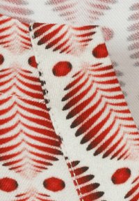 Gros plan sur un tissu avec des motifs en chevrons rouges et noirs et des pois sur un fond blanc, montrant des détails pliés et cousus.