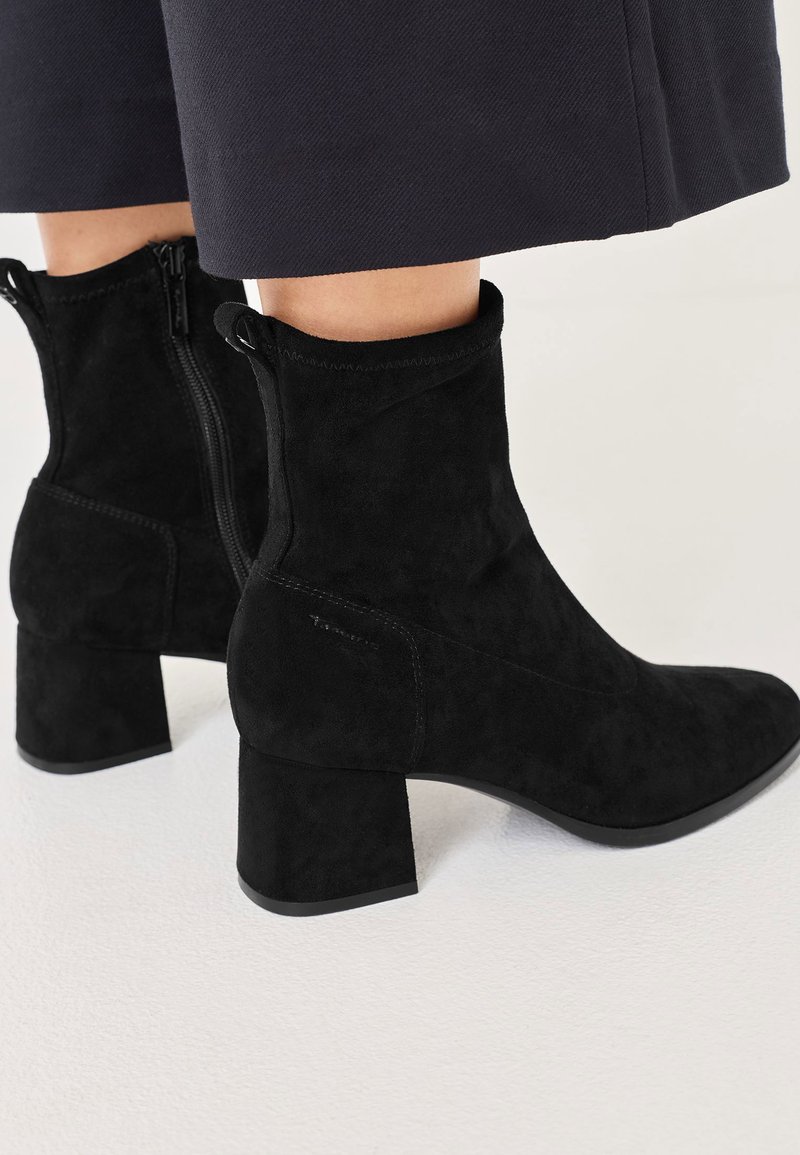 Crne nubuk čizme do gležnja s blok potpeticom, sa bočnim zatvaračem i čistim linijama. Tekstura je meka i glatka bez vidljivih uzoraka.