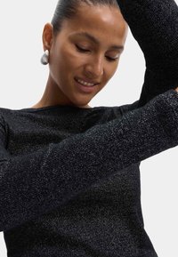 Schwarzes Langarmshirt aus strukturiertem Stoff mit metallischem Glanz. Verfügt über einen weiten Ausschnitt und enganliegende Ärmel, die eine schimmernde Oberfläche präsentieren.