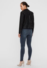 Black leather biker jacket with textured sleeves, fitted design, and silver hardware accents. Paired with dark denim skinny jeans and beige heels.