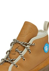 Brown leather high-top shoe with cream laces, textured surface, embossed monkey logo on the tongue, and a blue circular tag on the side.