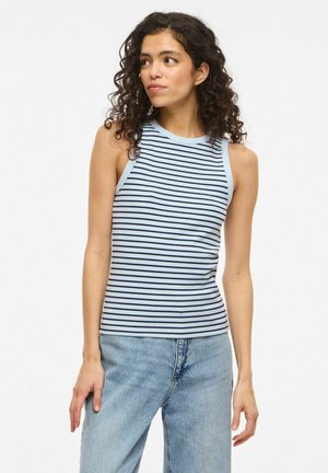 Femme aux cheveux bouclés portant un haut sans manches rayé bleu clair et noir et un jean bleu clair, regardant vers sa droite.