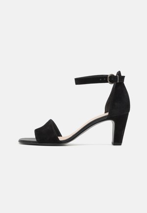 Sandales à talons en daim noir avec une bride au cheville, un bout ouvert et un talon noir brillant. Le design présente une texture douce et des accents minimaux.