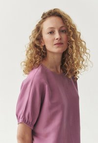 Blusa corta a maniche corte di colore viola chiaro con scollatura tonda e accenti arricciati sulle maniche, realizzata in morbido tessuto testurizzato.