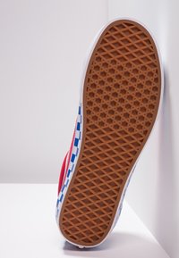 Červená plátěná skate bota s modro-bílým kostkovaným vzorem na boku a texturovanou hnědou gumovou podrážkou, s nízkoprofilovým designem.