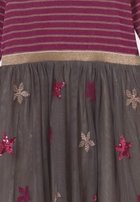 Mörkröd och guldrandig klänning med ett lager av grå tylskjol, prydd med rosa och guld stjärnformade paljetter.