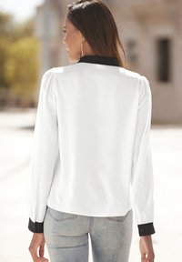 Witte blouse met lange mouwen en zwarte kraag en manchetten, met een soepele textuur en gathered details op de schouders, gedragen met lichtblauwe spijkerbroek.