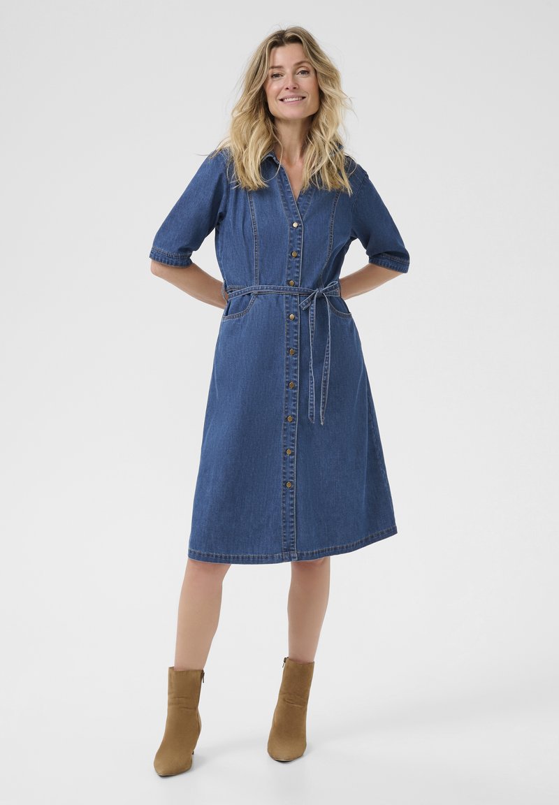 Denim obleka s kratkimi rokavi, gumbom ob sprednji strani, pasom na vezanje v pasu in dolžino do kolen. Izdelana iz modrega denima z gladko površino.