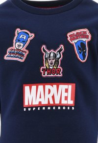 Marineblaue T-Shirt mit bunten gestickten Aufnähern von Superhelden: Captain America, Thor und Black Panther, mit einem weißen "MARVEL" Logo.