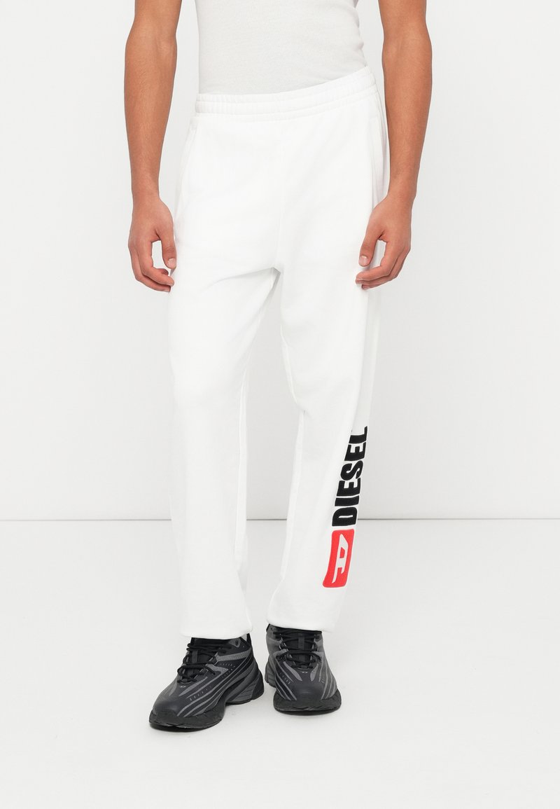 Λευκή φόρμα με ελαστική μέση και πλαϊνές τσέπες. Διαθέτει λογότυπο «DIESEL» σε μαύρο και κόκκινο χρώμα στο αριστερό πόδι.