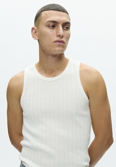 Hvit ribbestrikket tanktopp laget av bomull, med rund hals og ermeløs design, kombinert med lyse denimjeans.