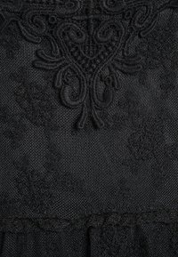 Prenda de encaje negro con intrincados bordados florales y patrones texturizados, con un diseño de dobladillo escalonado y tela suave y liviana.