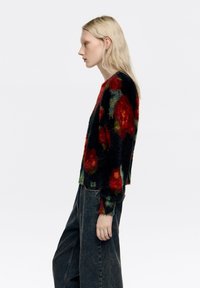 Puszysty czarny sweter z kolorowym kwiatowym wzorem w kolorach czerwonym, zielonym i żółtym. Posiada długie rękawy i krótki dół. Połączony z ciemnymi dżinsami.