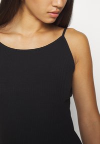 Débardeur noir à côtes avec fines bretelles. Le tissu a une texture lisse et un design ajusté, mettant en valeur un style minimaliste.