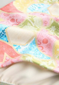 Tissu coloré présentant des motifs géométriques en rose, bleu, vert et jaune avec des designs complexes. Texture lisse ; bords finis.