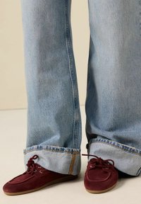 Hellblaue Jeans im Weitbein-Stil mit umgeschlagenen Säumen, kombiniert mit kastanienbraunen Wildleder-Slippern mit Schnürsenkeln und zwei silbernen Ösen.