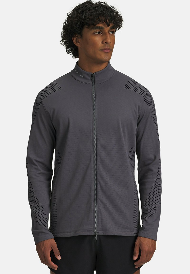 Man wearing a gray full-zip athletic jacket with perforated patterns on shoulders and sleeves, standing against a plain background.