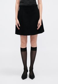 Μαύρη φουστάνι με φουσκωτό τελείωμα και μπροστινές τσέπες, λείο ύφασμα, σε συνδυασμό με διάφανα μαύρα γόνατα ψηλά καλσόν και μυτερά φλατ παπούτσια.