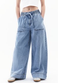 Vaaleansiniset farkkuleggingsit, joissa on joustava vyötärö, nyöri ja kaksi etutaskua; näkyvät saumat ja rento leikkaus.