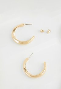 Gold-tone metal hoop earrings with a smooth, reflective surface, featuring a curved design and stud closure for secure wear.