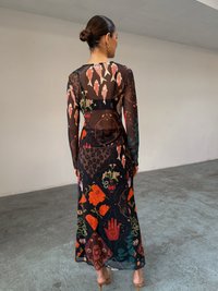 Μακρύ, διαφανές φόρεμα με περίπλοκα σχέδια που περιλαμβάνουν ψάρια, λουλούδια και γεωμετρικά σχήματα σε ζωηρά χρώματα πάνω σε μαύρο φόντο.