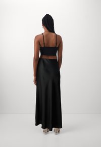 Jupe maxi en satin noir associée à un crop top noir ajusté. Texture lisse, fines bretelles et design épuré complètent la tenue.