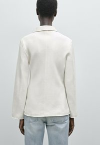 Cremfarbener Blazer mit strukturiertem Kragen, langen Ärmeln und Nahtdetails, kombiniert mit hellblauen Jeans. Strukturierter Stoff.